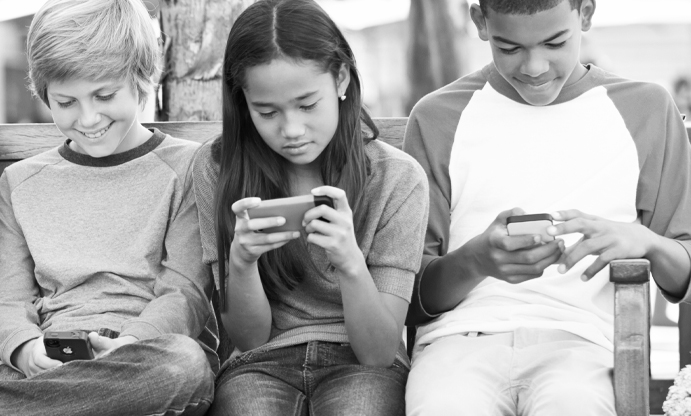 image of three young kids sitting using smart devices.