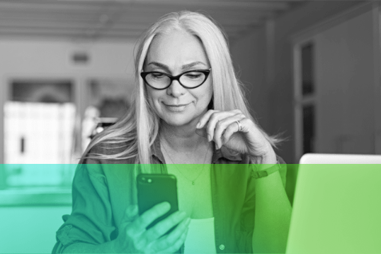 image of older woman wearing glasses sitting at table on phone.