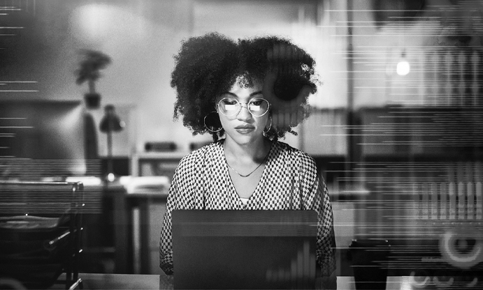 image of woman sitting at desk using a computer. The woman is wearing glasses.