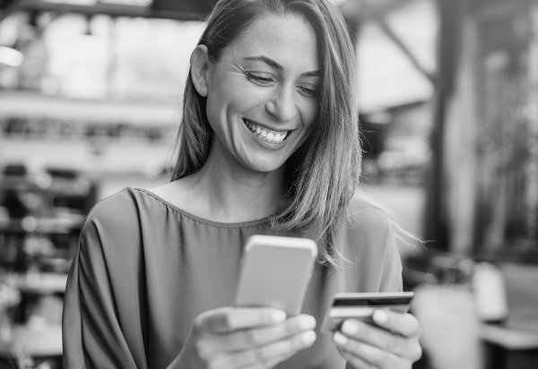 image of woman smiling. The woman is holding a card in her left hand and a smart phone in her right hand.