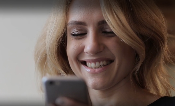 image of woman with short blonde hair smiling at her smart phone device.