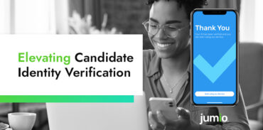 image of person smiling holding smart phone while looking at computer. Image shows Jumio's Thank you screen on right-hand side. Text on image reads: Elevating Candidate Identity Verification