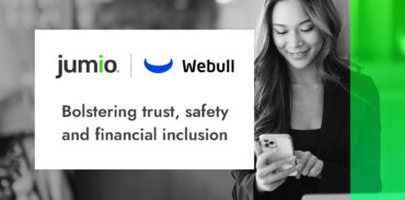 image of woman in background holding smart device. Webull logo and Jumio logo. Text reads: bolstering trust, safety and financial inclusion with Jumio.