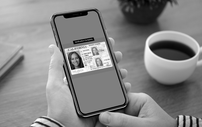 image of smart phone showing drivers licenses with cup of coffee to the right. Image is in black and white.