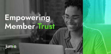 image of women wearing glasses holding phone in hand and smiling at computer. Image text reads: Empowering Member Trust.