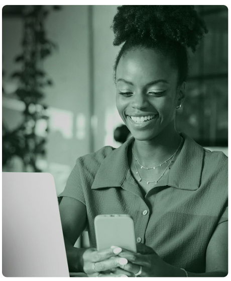 image of woman holding smart phone and sitting in front of a computer. Image has a green overlay.